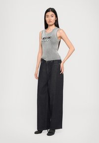 Γκρίζο ριμπ μακρυμάνικο τοπ χωρίς μανίκια με μαύρο κείμενο "Moschino Jeans" σε συνδυασμό με υπερβολικά φαρδιά σκούρα τζην παντελόνια. Το μοντέλο φοράει μαύρα τακούνια.