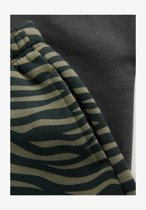 Tela a rayas verde y beige con un patrón de tigre junto a un textil liso de color gris oscuro, ambos mostrando texturas distintas.