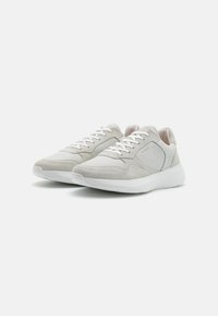 Zapatillas de ante y cuero gris claro con suelas blancas, que cuentan con un diseño curvado y acentos perforados en los lados.