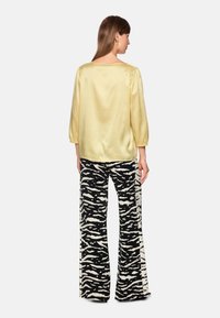 Yellow satin top with three-quarter sleeves paired with black and white zebra-striped flared pants. The look has a smooth texture and bold pattern.