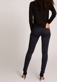 Jeans ajustados de color navy con una cintura de media altura, con bolsillos traseros acentuados. Combinados con una blusa negra ajustada y zapatos de tacón negros.