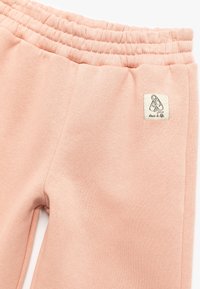 Jasnoróżowe dresy z gumką w talii, z małą naszywką w kształcie kwadratu oraz gładką, miękką tkaniną.