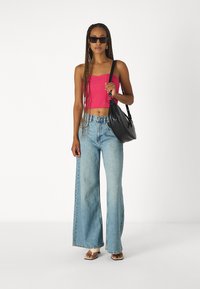 Ružový rebrovaný crop top, svetlomodré široké nohavice, čierna kabelka na rameno, ploché sandále, tmavé slnečné okuliare, copy, minimalistické pozadie.