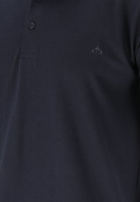 Marineblauw poloshirt met zwarte knopen en een klein geborduurd geometrisch logo op de linkerborst.
