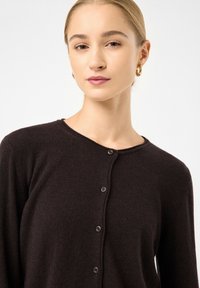 Dunkelbrauner Cardigan aus softem Strickmaterial, mit Rundhalsausschnitt, langen Ärmeln und Knöpfen zum Schließen vorne.