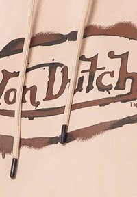 Sweat à capuche beige avec un design graphique brun portant le texte "Von Dutch", cordons de serrage avec des embouts foncés. Texture douce, style décontracté.
