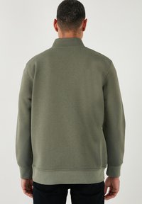 Pulover verde măsliniu cu guler, mâneci lungi, tivuri și manșete ribbate. Textură netedă cu un design minimalist.