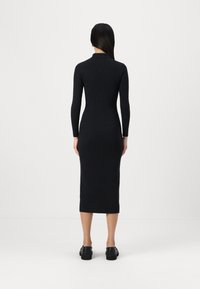 Abito nero a coste con maniche lunghe e scollatura alta, aderente fino alla caviglia. Tessuto liscio e design minimalista.