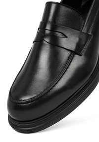 Mocasines de cuero negro con un acabado suave, que presentan una tira decorativa en el empeine y un diseño de puntera redondeada. Detalles de costura sutil.