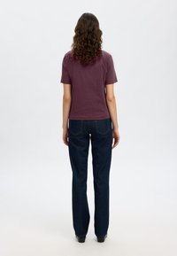 Camicia a maniche corte di colore bordeaux abbinata a jeans dritti blu scuro, mostrata da dietro, con una vestibilità comoda e un design semplice.