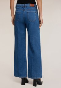 Vuoristavat siniset farkut, joissa on korkea vyötärö, kaksi takataskua ja ruskea nahkatägi vyötärönauhan kohdalla. Sileä pinta.