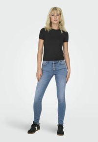 Svart kortärmad t-shirt i kombination med ljusblå högmidjade skinny jeans med femknapps stängning och svarta sneakers med beige sula.