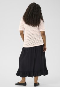 Light pink, knitted top with short sleeves and a diamond pattern, paired with a black, floor-length skirt featuring a ruffled hem. Black flats.