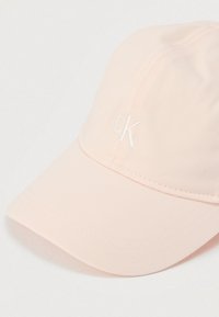 Ροζ καπέλο μπέιζμπολ με καμπυλωτό γείσο, κατασκευασμένο από ελαφρύ ύφασμα. Διαθέτει κεντημένο λογότυπο "cK" σε λευκό στο μπροστινό μέρος. Υφή επιφάνειας.