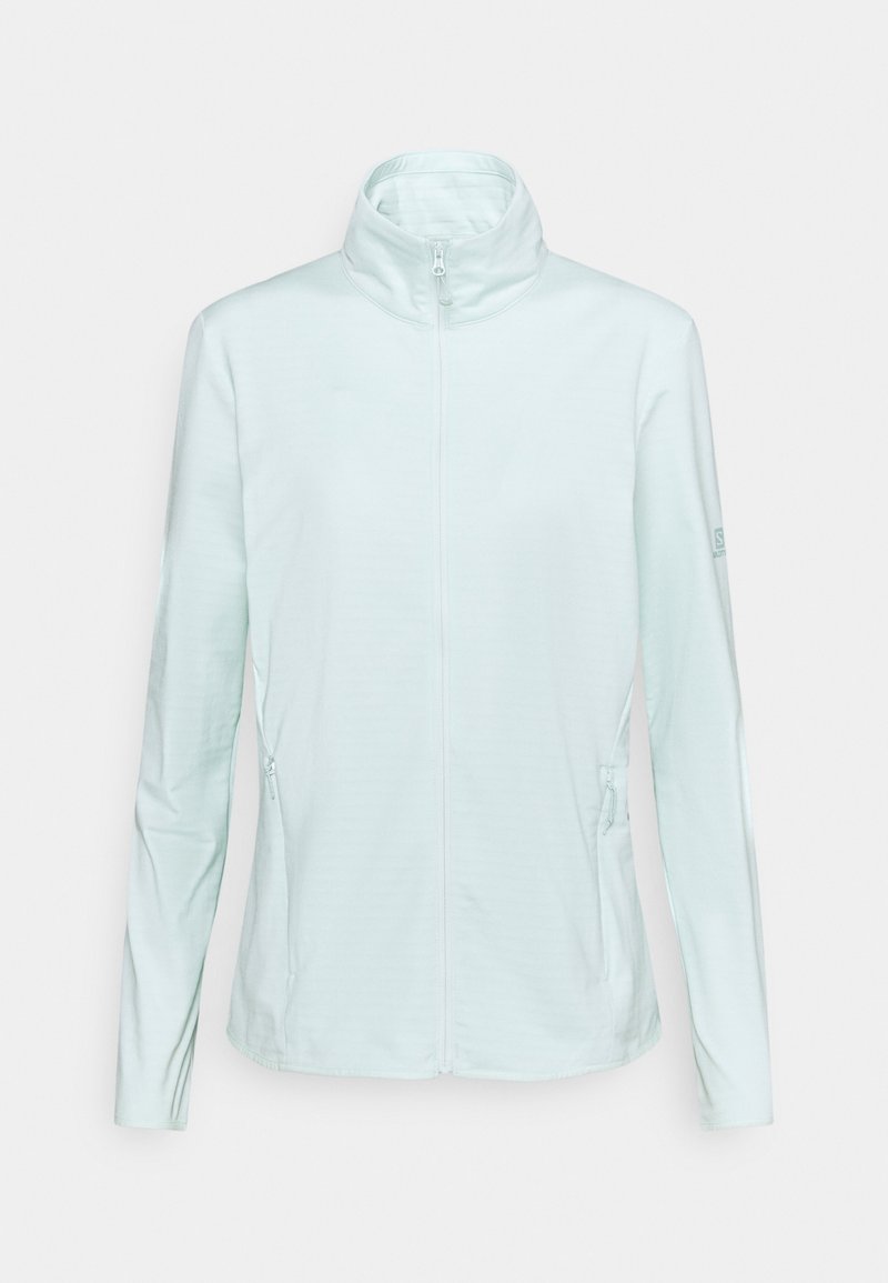 Veste softshell bleu clair avec fermeture éclair intégrale sur le devant, col montant, manches longues et poches latérales zippées, présentée sur fond blanc uni.