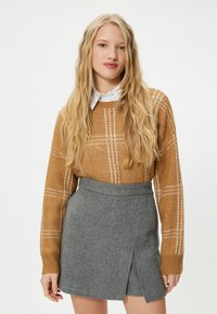 Braun kariertes Sweatshirt mit langen Ärmeln, kombiniert mit einem grauen Woll-Minirock mit einem Schlitz vorne. Glatte Textur und figurbetonter Schnitt.