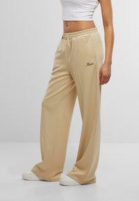 Béžové široké teplákové nohavice z jemného materiálu, s elastickým pásom, bočnými vreckami a vyšívaným logom.