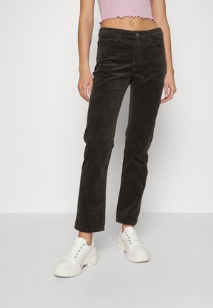 Persoon draagt zwarte corduroy broek, witte chunky sneakers en een cropped roze mouwloos topje tegen een effen lichte achtergrond.