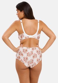 Femme vue de dos portant un soutien-gorge blanc et des culottes taille haute à motifs floraux avec des fleurs rose et verte, les mains sur les hanches.
