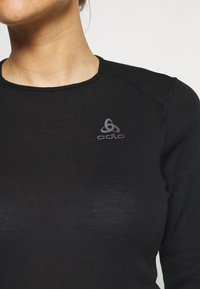 Svart långärmad topp i ribbat material med rund halsringning och en liten grå Odlo-logotyp på vänster bröst.