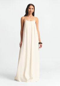 Cremefarvet maxikjole med tynde spaghetti-stropper, afslappet pasform og blødt, flydende stof. Har en indsamlet bodice og minimale detaljer.