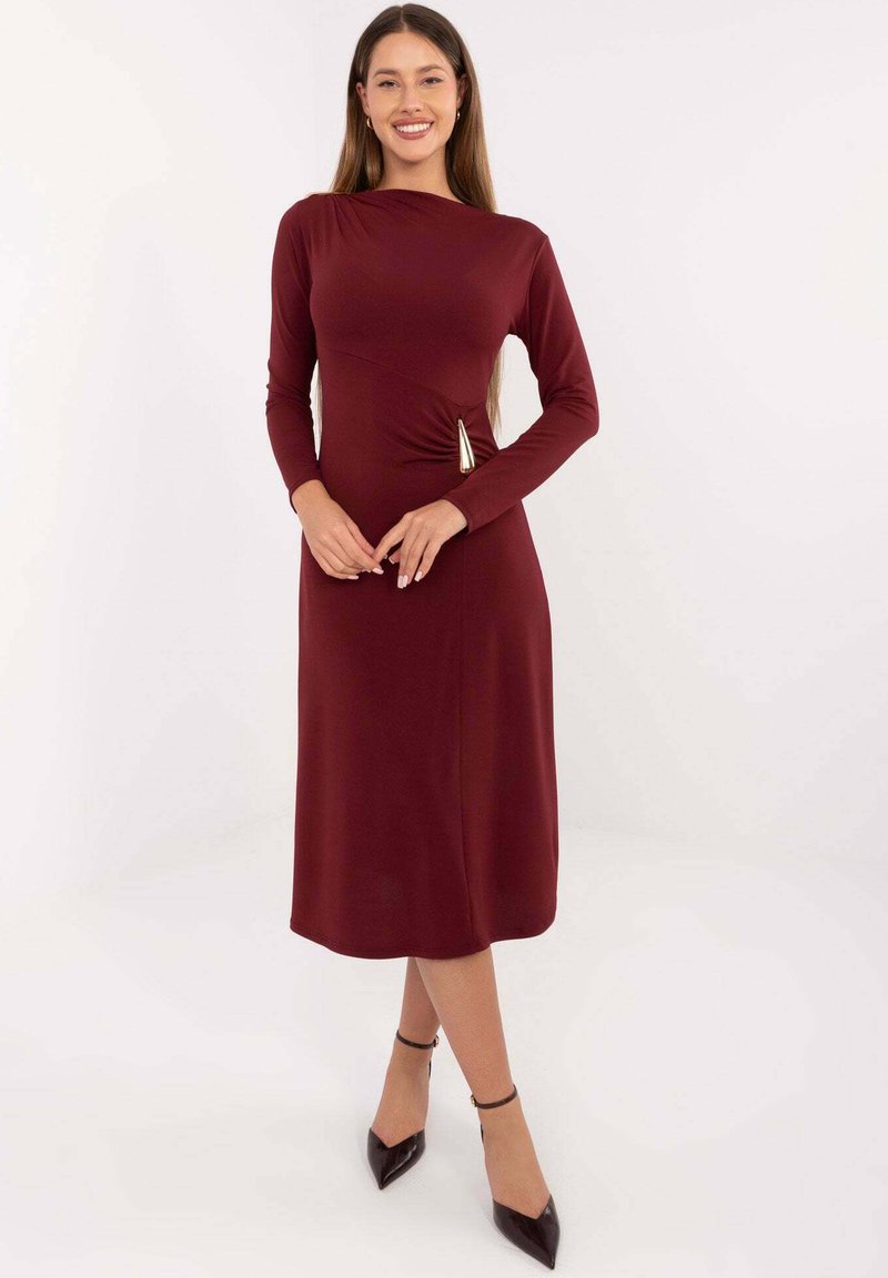 Bordowa sukienka z długim rękawem o dopasowanym kroju, asymetrycznym dekolcie i bocznych ozdobach. Gładka faktura, długość do połowy łydki.