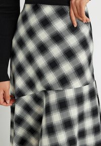 Jupe à carreaux noir et blanc avec une taille haute, présentant un design superposé et des poches, fabriquée à partir d'un tissu lisse avec un motif en grille.