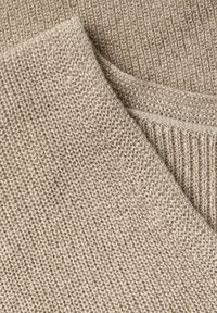 Beige pletená látka s texturovaným vzorem. Má měkký, mírně lesklý vzhled díky akcentu z metalického vlákna. Okraje jsou hladké a dokončené.