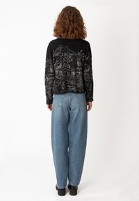 Svart tröja med invecklade vita mönster som föreställer byggnader och natur, ihop med ljusblå vida jeans, bärs med svarta platåskor.