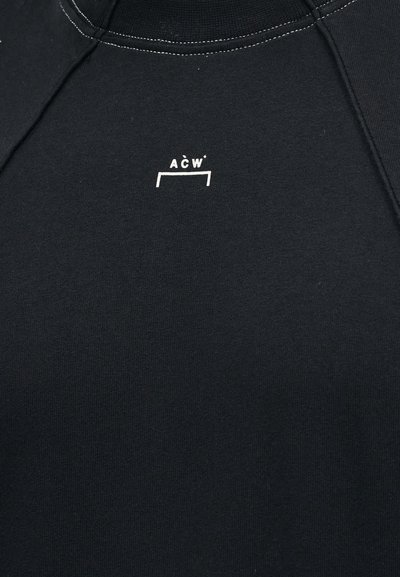 Κοντινή λήψη μαύρου υφάσματος με λευκό λογότυπο ACW και λεπτομέρεια ραφής κοντά στο πάνω κέντρο.