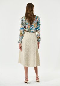 Bluse mit Blumenmuster und langen Ärmeln, kombiniert mit einem strukturierten, knielangen Rock in Cremefarbe. Verfügt über eine taillierte Taille und einen natürlichen Saum.