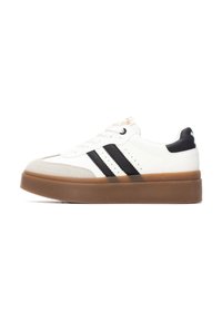 Zapatilla blanca con rayas negras, con punta redondeada y suela gruesa de goma marrón. Detalles texturizados en la punta y el talón.