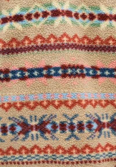 Pehme beež riie, millel on horisontaalsed read punase, sinise ja rohelise geomeetrilise ja sakilise mustriga.