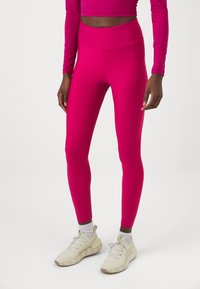 Leggings atletici aderenti di un vivace rosa, realizzati in un materiale liscio e elastico con una vita alta. Abbinati a sneakers color crema.