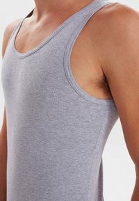 Grå tanktop lavet af blødt, struktureret bomuld. Har en rund halsudskæring og brede ærmeåbninger, tætsiddende design der fremhæver torsoen.