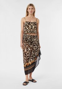 Schwarzes und sandfarbenes gemustertes Crop-Top mit dünnen Trägern, kombiniert mit einem luftigen Rock mit einem ähnlichen Design und einem asymmetrischen Saum. Schwarze Sandalen.