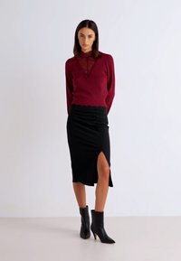 Bordeaux trui met kantdetails, gecombineerd met een zwarte geribbelde rok met rimpeling en een zijsplit. Zwarte enkellaarsjes maken de look af.