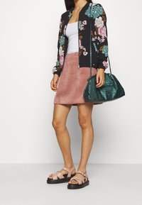 Giacca bomber floreale con base nera, gonna in corduroy rosa, borsa texturizzata teal e sandali rosa chiaro con cinturini regolabili e suole nere.