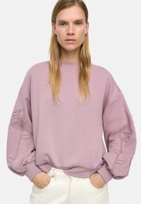 Jasnoróżowy sweter z balonowymi rękawami, z haftowanym wzorem róży na lewym rękawie oraz ribbowym dekoltem i mankietami.