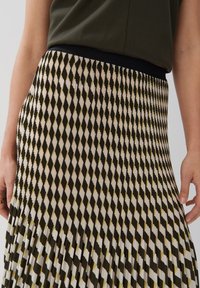 Gonna plissettata con un motivo geometrico in bianco, nero e oliva. Presenta una vita elastica nera e una texture di tessuto fluido e leggero.