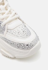 Sneaker blanche avec tige en mesh ornée de strass argentés. Présente un bout rond, une semelle texturée et des lacets plats blancs.