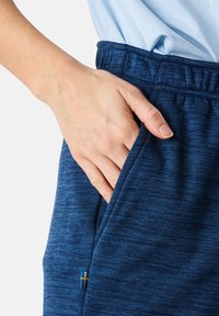 Marina atletiska shorts gjorda av texturerat tyg, med elastisk midja och sidofickor. En liten gul och blå detalj är synlig.