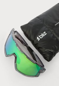 Óculos de sol com uma armação cinza e lentes verdes em degradê ao lado de uma capa preta acolchoada. A capa apresenta a marca "bliz" em branco.