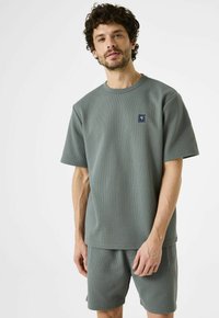 Grijze katoenen t-shirt met wafelstructuur en bijpassende shorts, ronde halslijn, korte mouwen en een klein logo-opdruk op de borst.