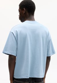 T-shirt di cotone azzurro chiaro con vestibilità comoda, maniche corte e orlo dritto. Tessuto liscio, design semplice, senza motivi o dettagli visibili.