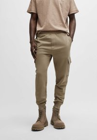 Khaki cargobyxor i sweatpantsstil med smal passform, elastisk midja, sidofickor och ribbade muddar, tillsammans med beige snörade stövlar.