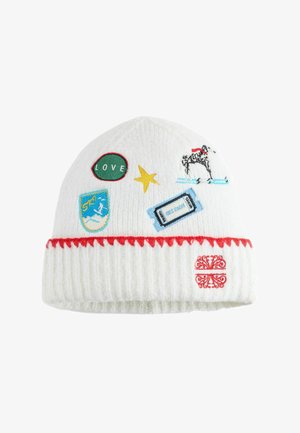 Valge kootud müts punase äärega, millel on plaastrid dalmaatsia koera, kollase tähe, suusamärgi, sõnaga "LOVE" ja sinise piletiga.