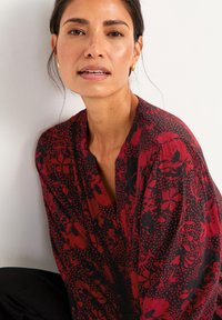 Rød og sort mønstret top lavet af letvægtsstof, prydet med blomsterdesigns, en V-halsudskæring og afslappede ærmer.