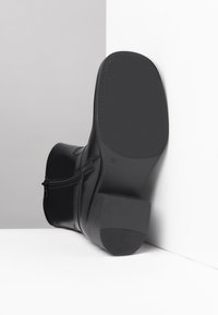 Stivaletto in pelle nera con punta arrotondata, zip laterale e suola in gomma testurizzata. Tacco leggero e finitura liscia con accenti minimi.