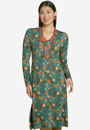 Grünes Blumenkleid mit langen Ärmeln, das mit orangefarbenen, lila und weißen Mustern versehen ist. V-Ausschnitt-Design, seitlicher Schlitz, kombiniert mit roten Perlenaccessoires.